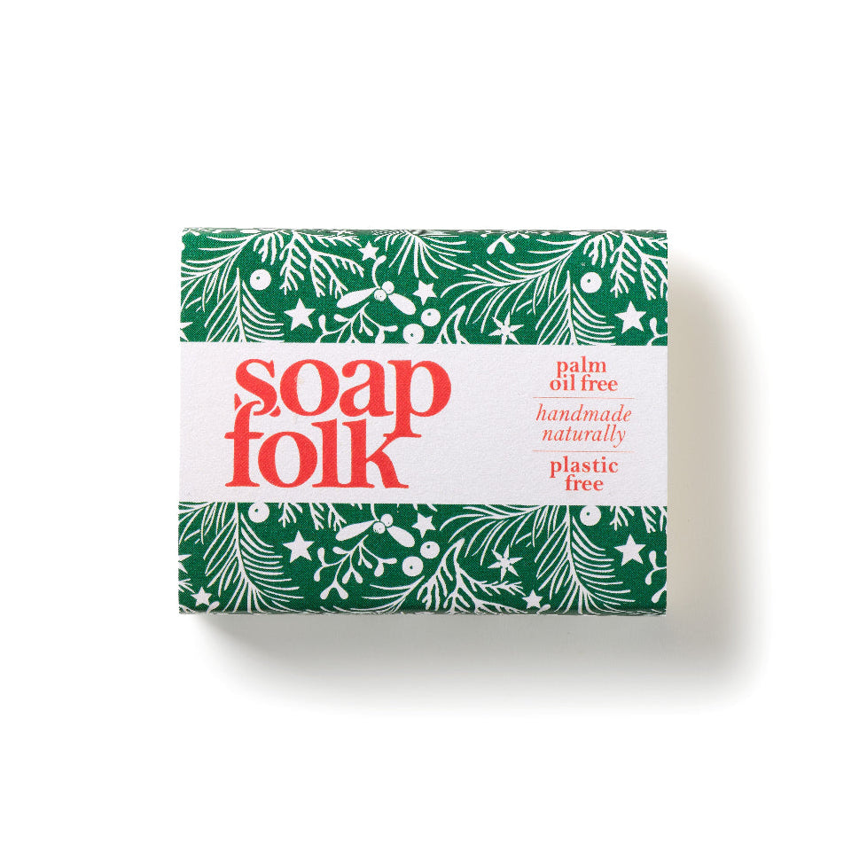 A rectangular bar of soap wrapped in a white paper band with green botanical borders and red text reading 'soap folk'.