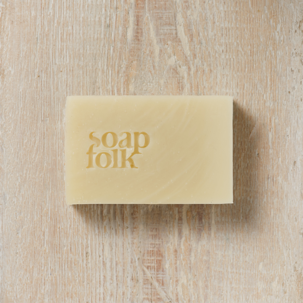 Unwrapped bar of Lavender and Oatmilk 
soap with 'soap folk' branding on a wooden surface