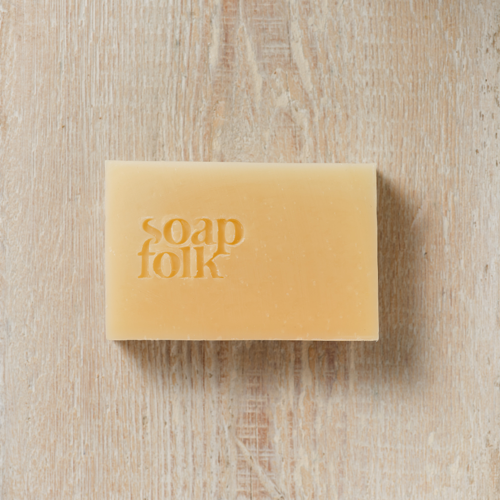 Unwrapped bar of  Lemon and Bergamot 
soap with 'soap folk' branding on a wooden surface