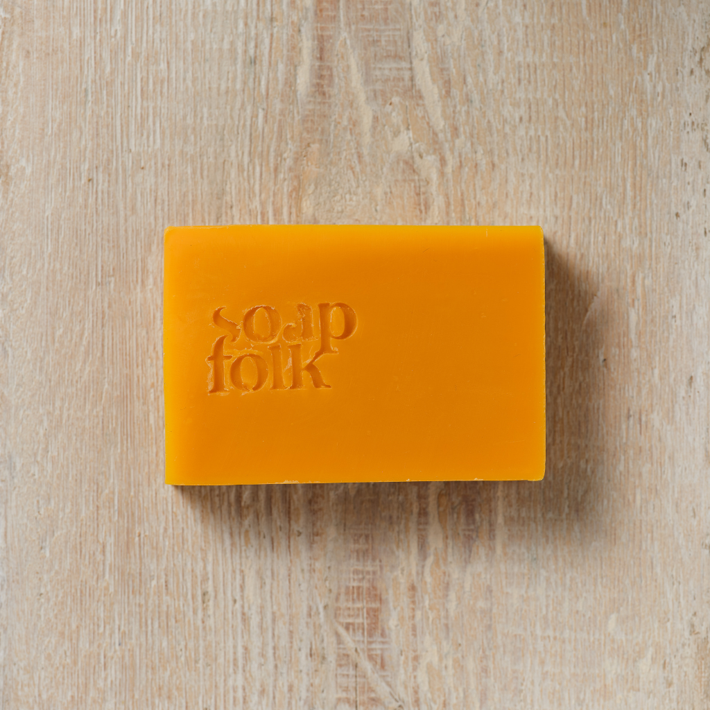 Unwrapped Orange and Ginger soap bar with 'Soap Folk' branding on a wooden surface