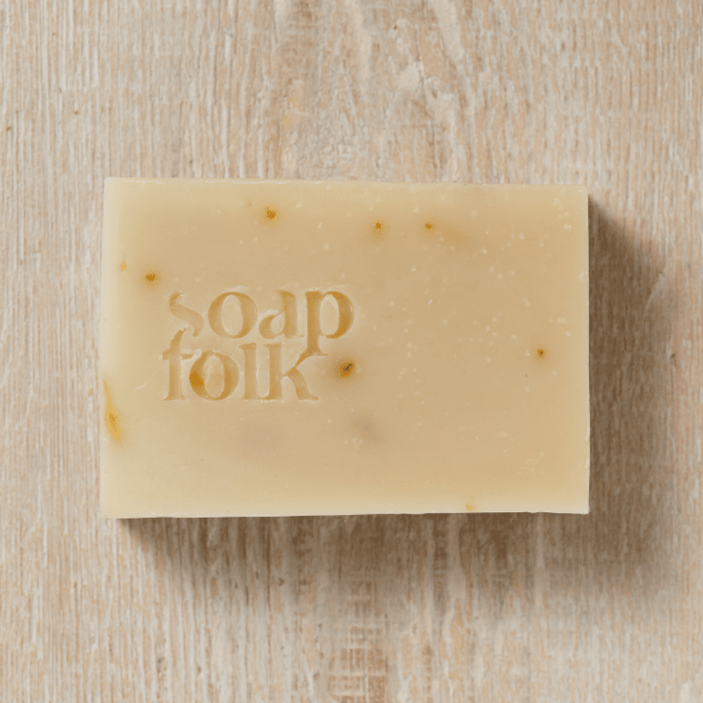 Bar of Calendula soap with 'soap folk' embossed in the bar. Sat on a wooden surface.